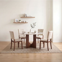 Unberto Two Tone Round Dining Table & Chairs Set A 5-piece dining set featuring a round white marble-top table with a dark wood pedestal base and four matching chairs with cream upholstery, styled on a woven rug against a warm beige wall.