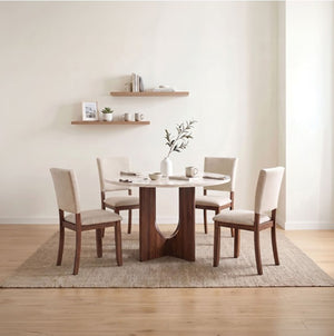 Unberto Two Tone Round Dining Table & Chairs Set A 5-piece dining set featuring a round white marble-top table with a dark wood pedestal base and four matching chairs with cream upholstery, styled on a woven rug against a warm beige wall.