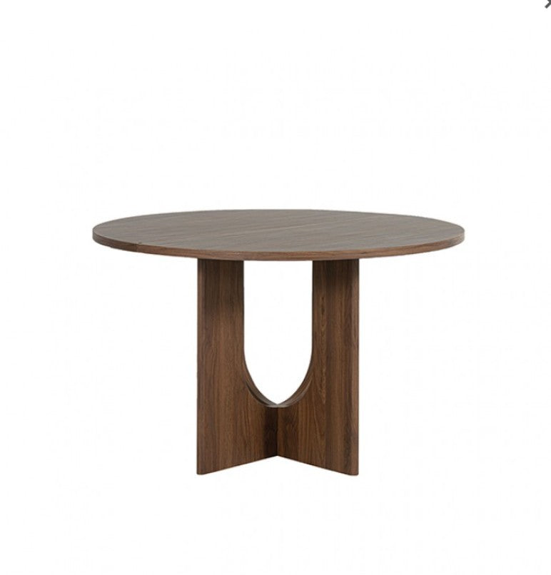 Unberto Walnut Round Dining Table A round wooden dining table with a sculptural pedestal base, surrounded by four gray upholstered dining chairs in a warm, neutral-toned dining room setting.