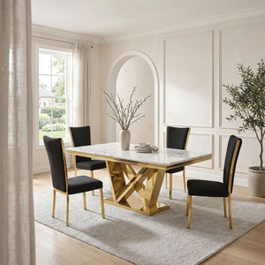 Valdi Gold White Sintered Stone Top Dining Table A modern dining room set featuring a rectangular marble-top table with a gold geometric base and four black upholstered chairs with gold legs, styled in a bright, elegant room with cream walls and wood floors.