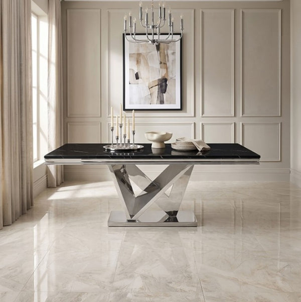 Valdi Silver Black Sintered Stone Top Dining Table A modern rectangular dining table with a glossy black top and a polished chrome geometric X-shaped pedestal base, styled in a bright, elegant dining room with beige paneled walls and marble floors.