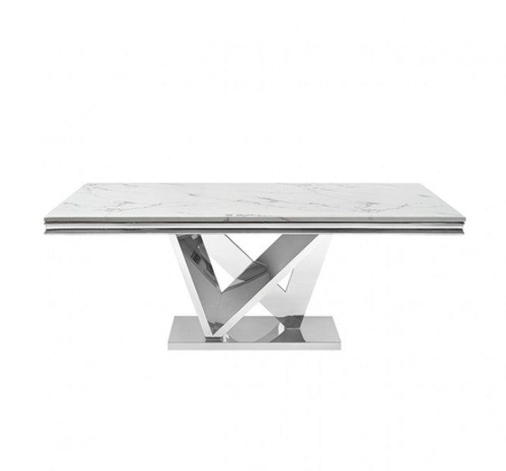 Valdi Silver White Sintered Stone Top Dining Table A modern rectangular dining table with a white marble-look top and a reflective chrome geometric pedestal base, styled in a bright room with beige paneled walls, a light rug, wood floor, and a hanging chandelier.