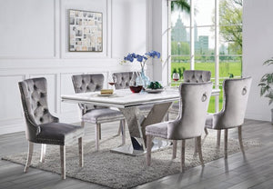 Valdi Silver White Sintered Stone Top Dining Table A 7-piece dining set featuring a rectangular white marble-top table with a chrome base and six tufted gray velvet chairs with silver nailhead trim, shown in a bright modern dining room.