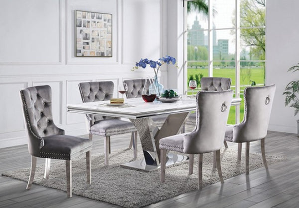 Valdi Silver White Sintered Stone Top Dining Table A 7-piece dining set featuring a rectangular white marble-top table with a chrome base and six tufted gray velvet chairs with silver nailhead trim, shown in a bright modern dining room.