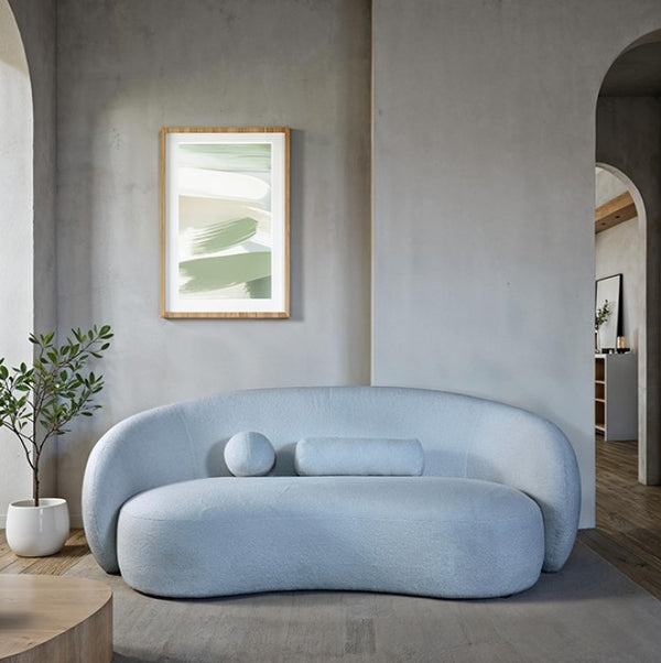 Vika Sofa Curved Back and Arm Powder Blue Modern light blue sofa in a minimalistic living room with a plant and framed artwork.