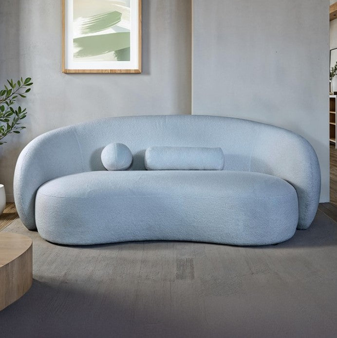 Vika Sofa Curved Back and Arm Powder Blue Modern light blue sofa in a minimalistic living room with a plant and abstract art on the wall.