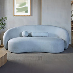 Vika Sofa Curved Back and Arm Powder Blue Modern light blue sofa in a minimalistic living room with a plant and abstract art on the wall.