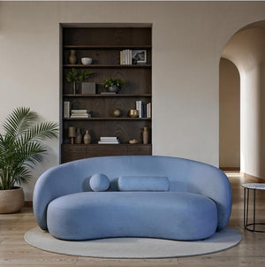 Vika Sofa Back and Arm Curved Denim Blue Modern blue sofa in a stylish living room with a bookshelf and plants.
