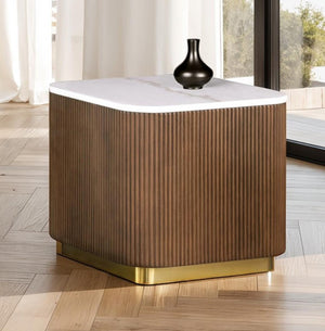 Wooden side table with white top and gold base in a room with large windows.