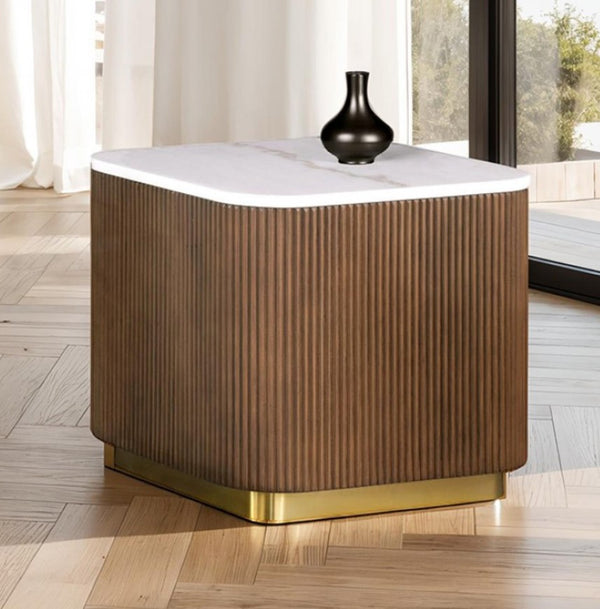 Wooden side table with white top and gold base in a room with large windows.