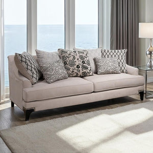 Welma Taupe Sloped Arms Sofa with Pillows Beige sofa with patterned cushions in a room with large windows and a lamp.